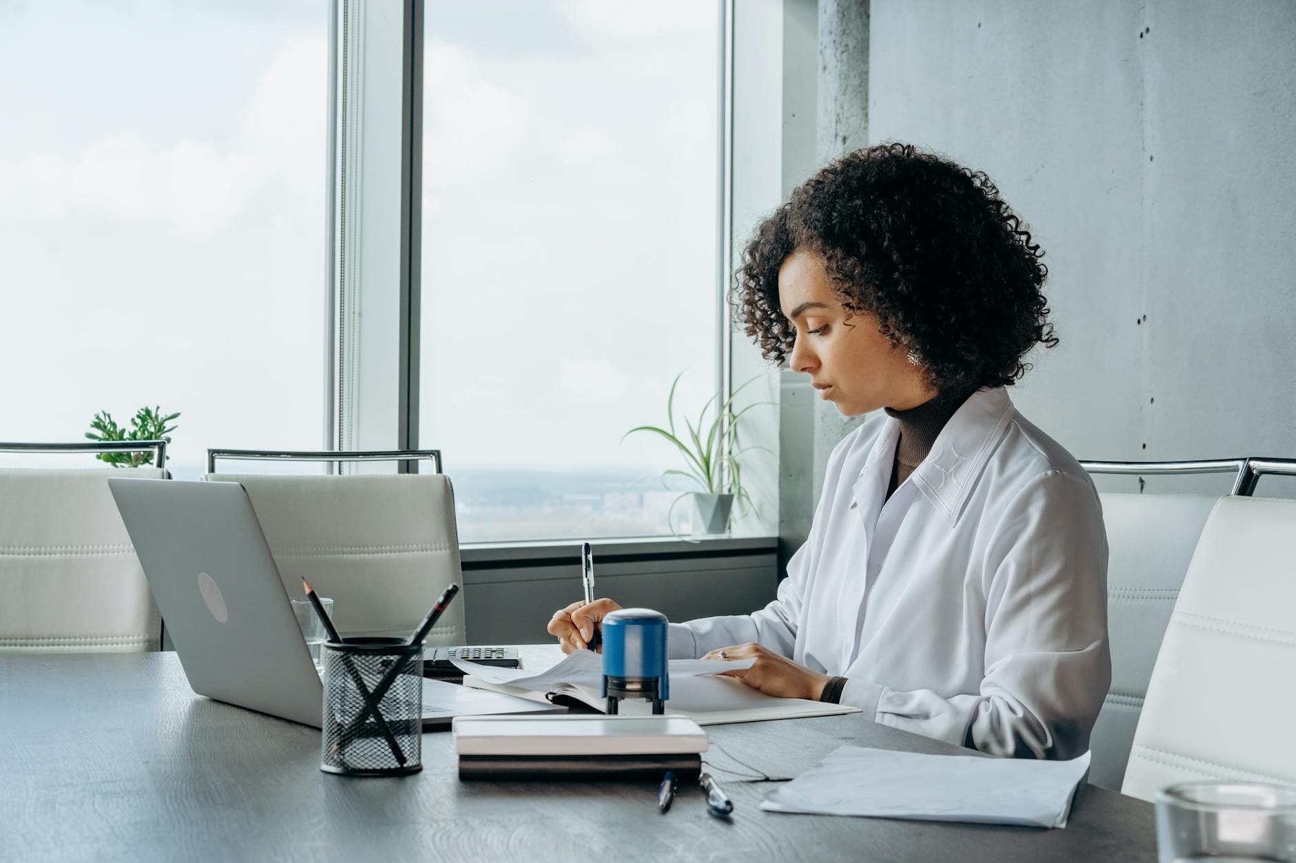 African American woman in a white shirt working at a laptop in a bright, modern office setting.