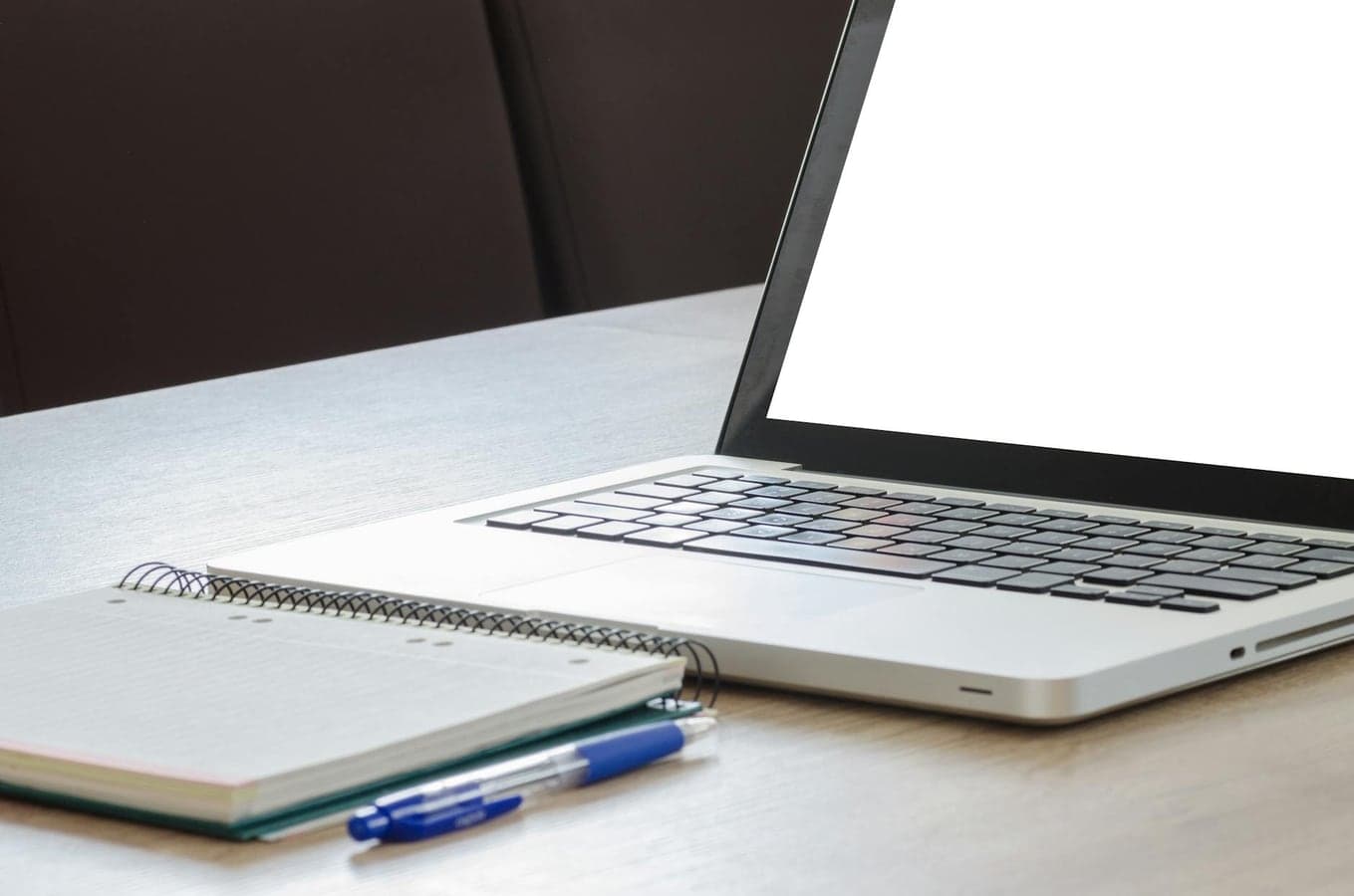 Open laptop with blank screen, notebook, and pen on a wooden desk, ideal for work or study.