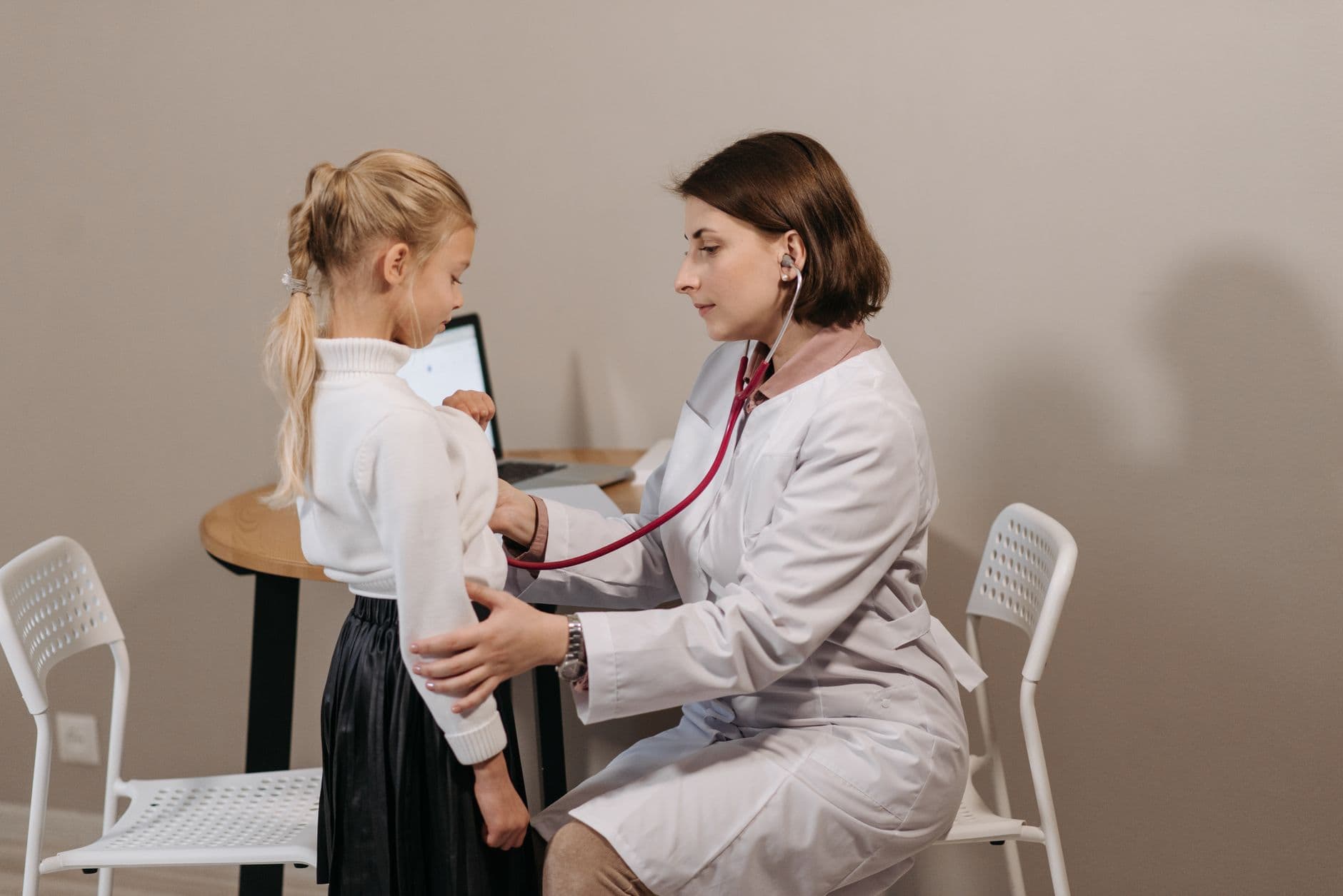 A pediatrician listens to a child's heartbeat during a check-up in a clinic setting.