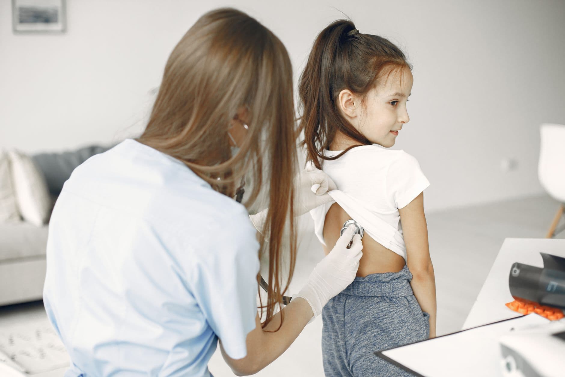A female doctor uses a stethoscope to examine a child in a medical examination room.