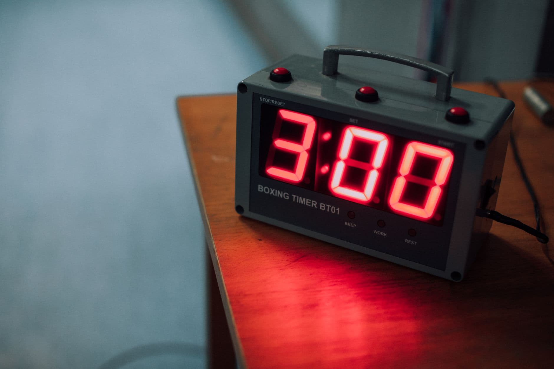 A digital boxing timer displaying 3:00 resting on a wooden table.